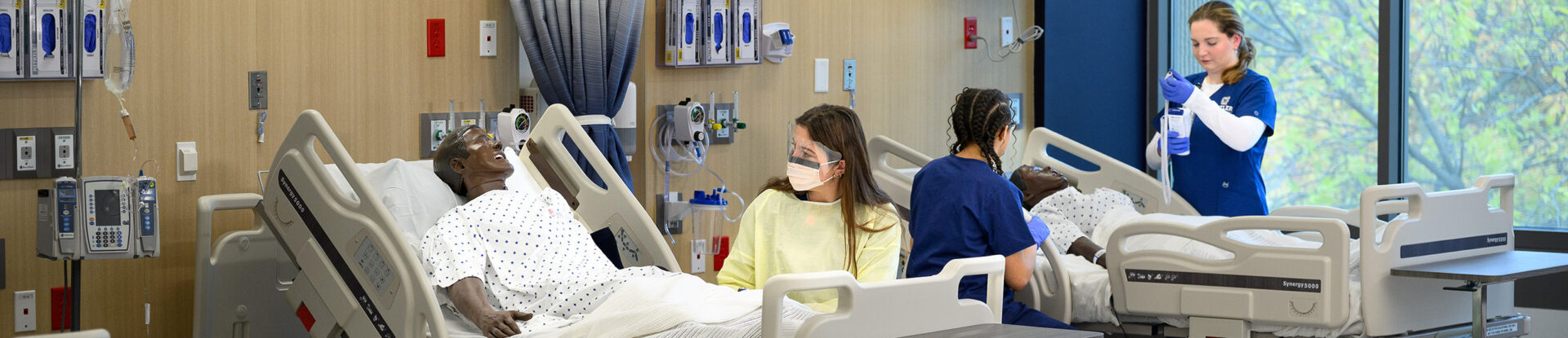 Nursing students work at hospital beds with manikin patients.