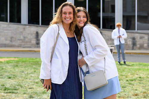 Female student in white medical coat leans into female parent for a photo.