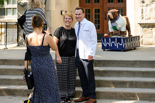 Male student in white medical coat poses for photo with female parent.