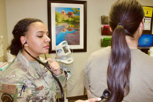 Aubrey Brown, wearing military fatigues, listens to a patient while using a stethoscope on her back.