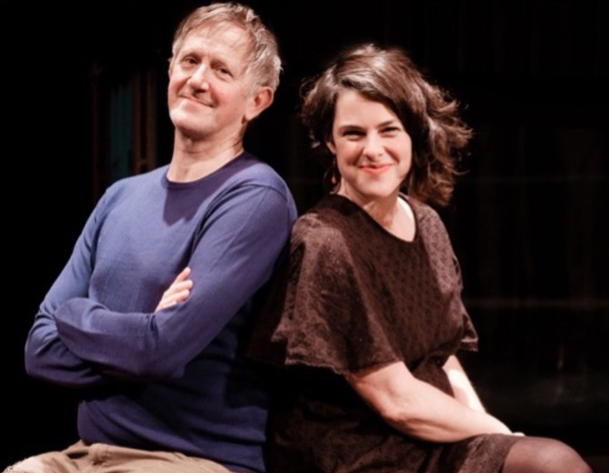 Performers Jos Houben and Emily Wilson smile back-to-back.