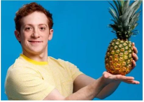 Ethan Slater in yellow shirt holding a pineapple.