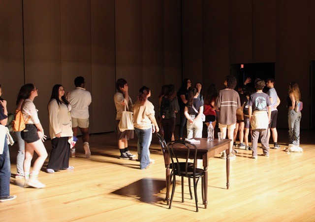 Students exploring stage area with prop table and chair on center stage.