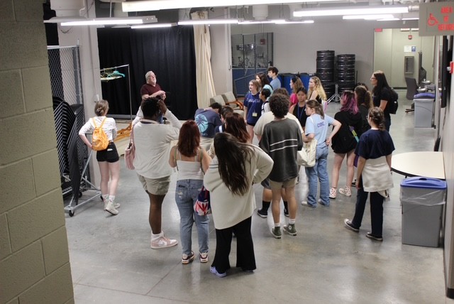 Students gather around instructor in backstage area.