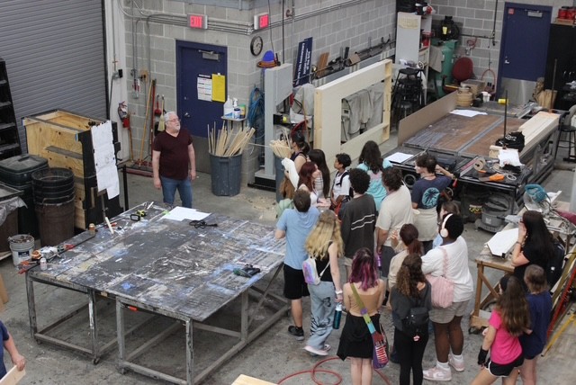 Students stand in art department to hear instructor explain prop creation.
