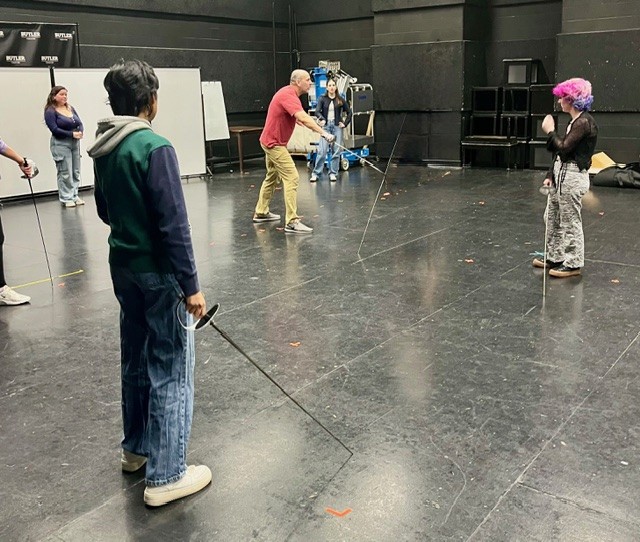 Students holding sword props while instructor shows how to wield one.