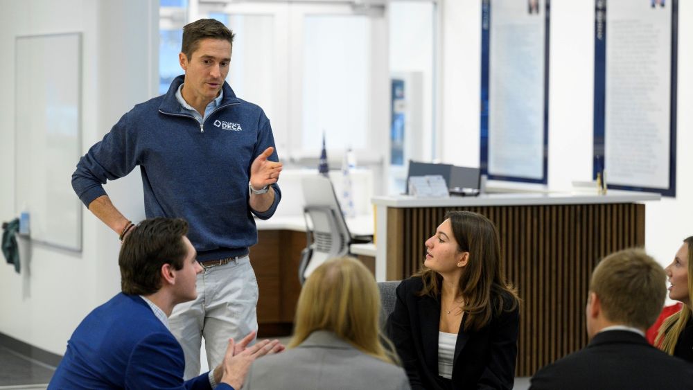 Photo of one person standing and speaking to a group of other people