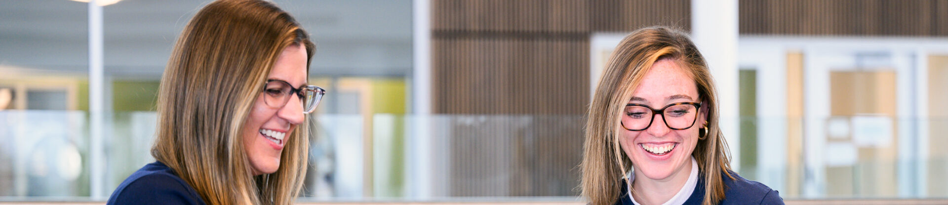 Two female business students smile while sitting in Dugan Hall.