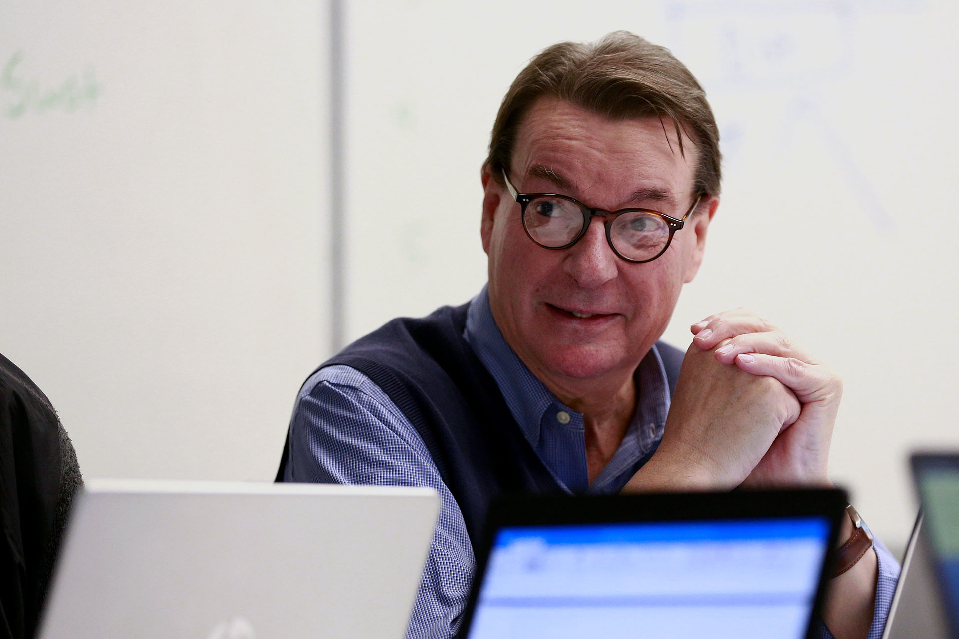 Man with glasses listening with laptops on conference room table.