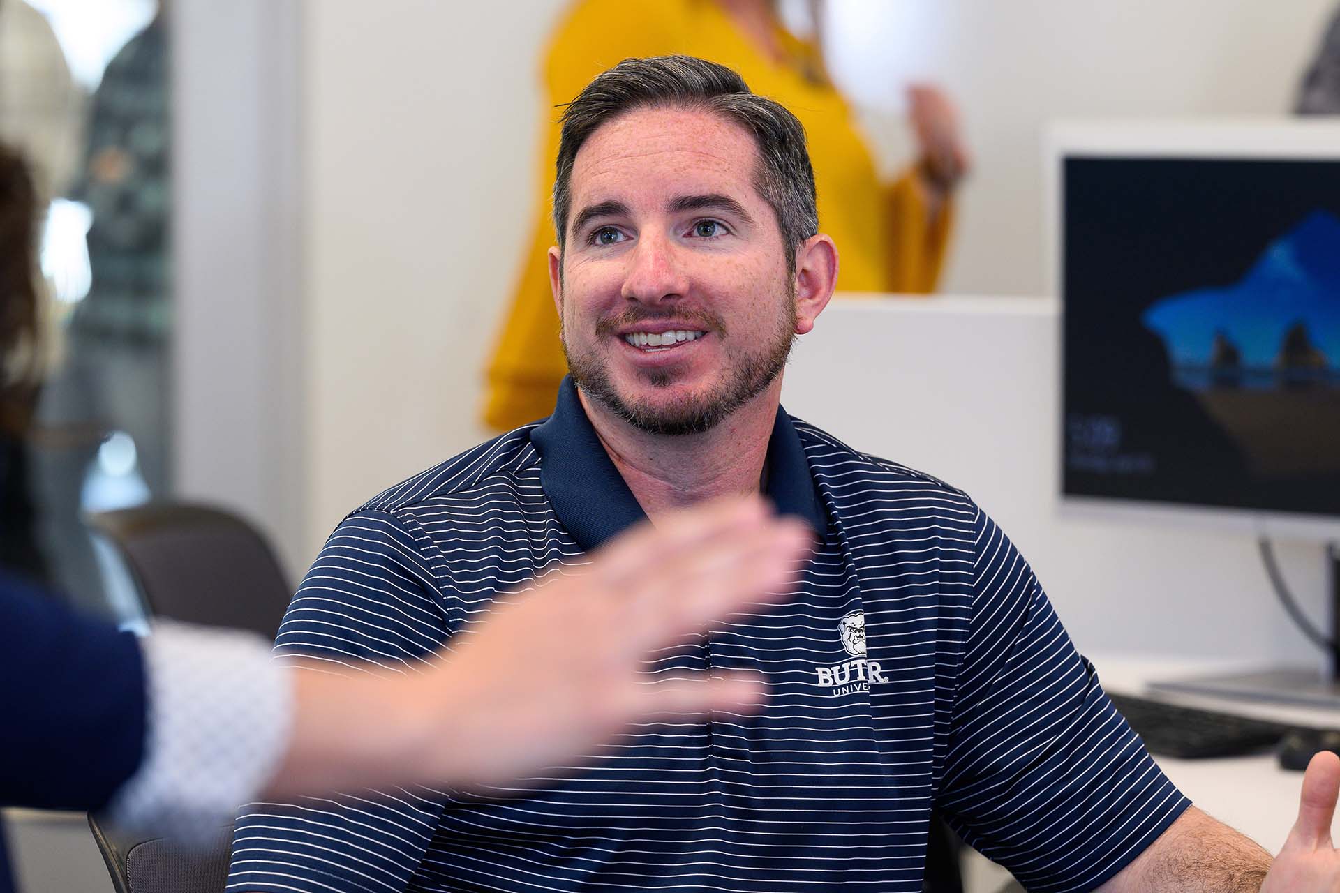 Man in Butler University striped polo shirt smiles while chatting with another MBA student.