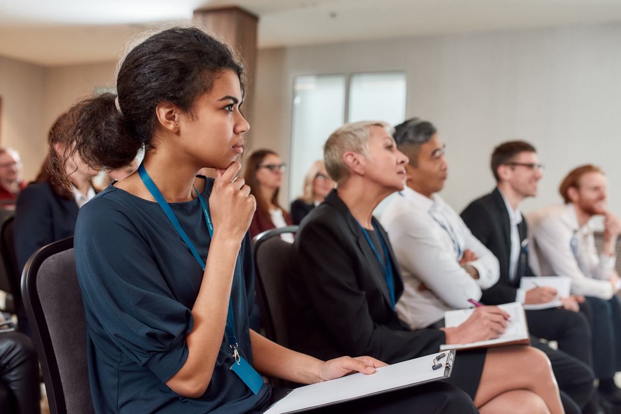 Students sitting in a row and making notes while listening to presentation at conference hall.