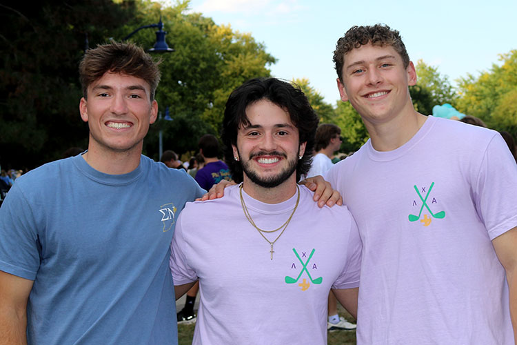Three men from fraternities stand in a group smiling.