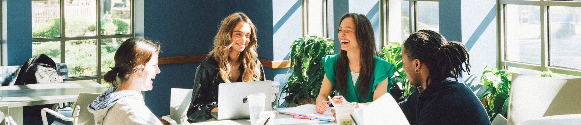 Four college students laughing at table in student union building.
