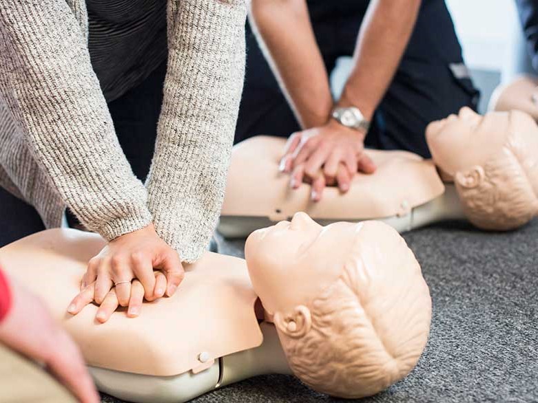 This is a photo of a CPR class. You can't see anyone's faces. Just hands pushing down on manikins.