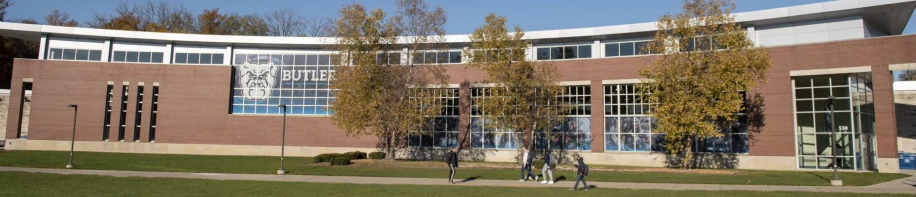 This is a wide photo of the front of the HRC facility. It is fall and several students are walking in front of the building. 