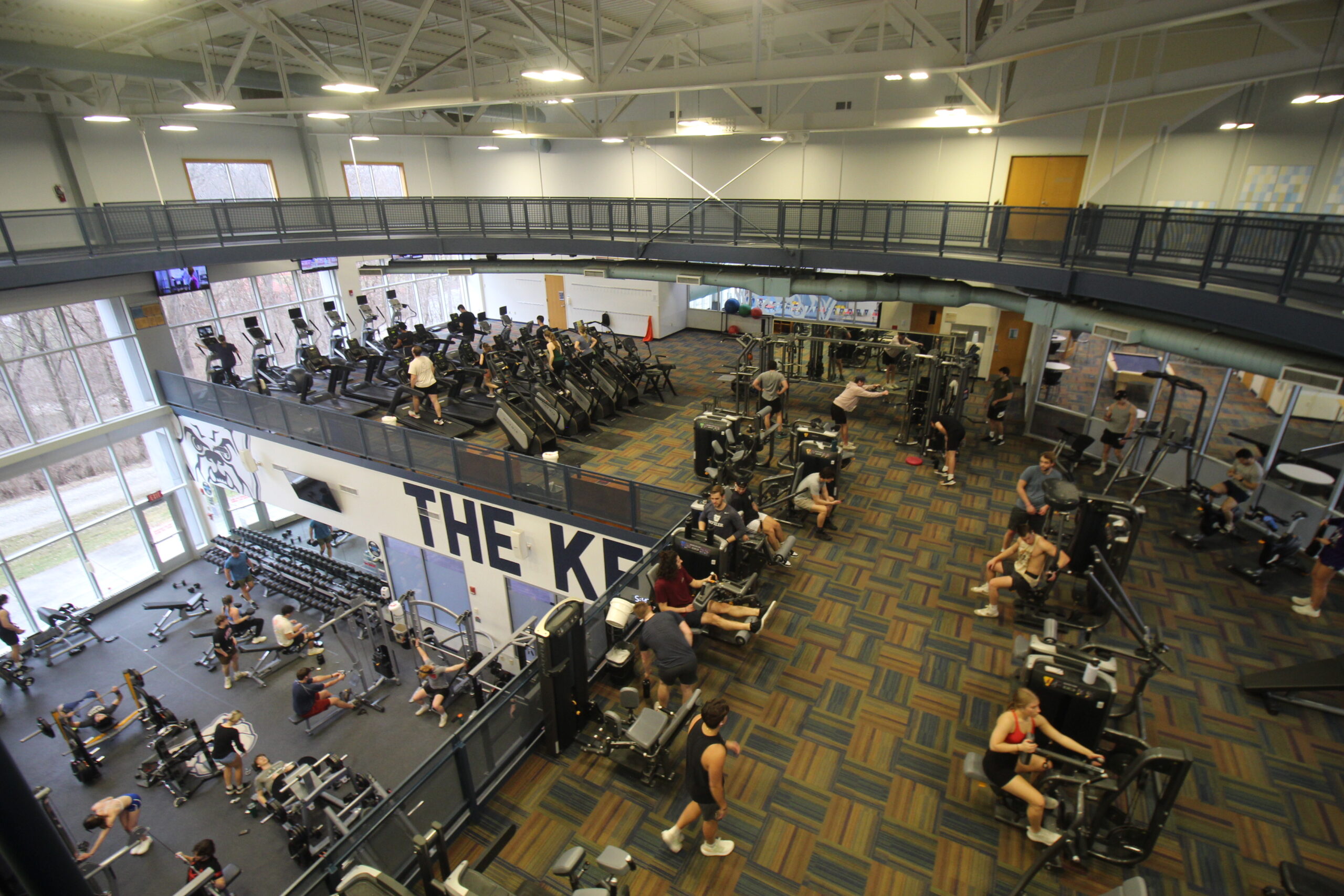 This is an arial photo of the 2nd floor of the recreation center. It shows many people working out on machines and lifting weights. 