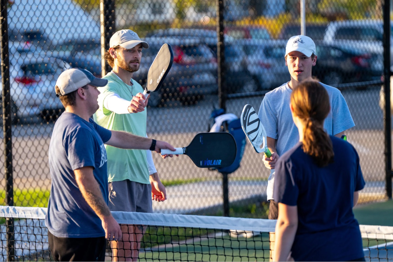 This is a photo of four people playing pickleball and tapping their paddles together above the net.
