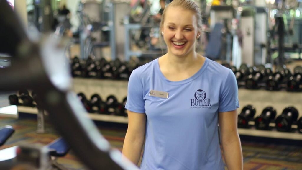 This is a photo of a lady in a blue shirt on the fitness floor smiling. 
