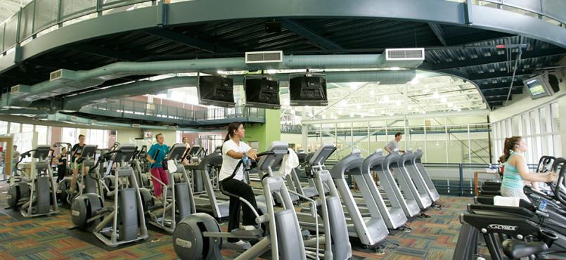 This is a photo of the machines and tread mills on the fitness floor. You can see on person using an elliptical machine. 