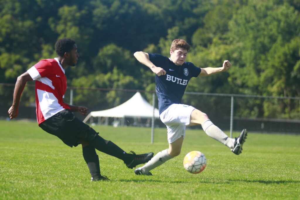 Two guys playing soccer on a grass field.