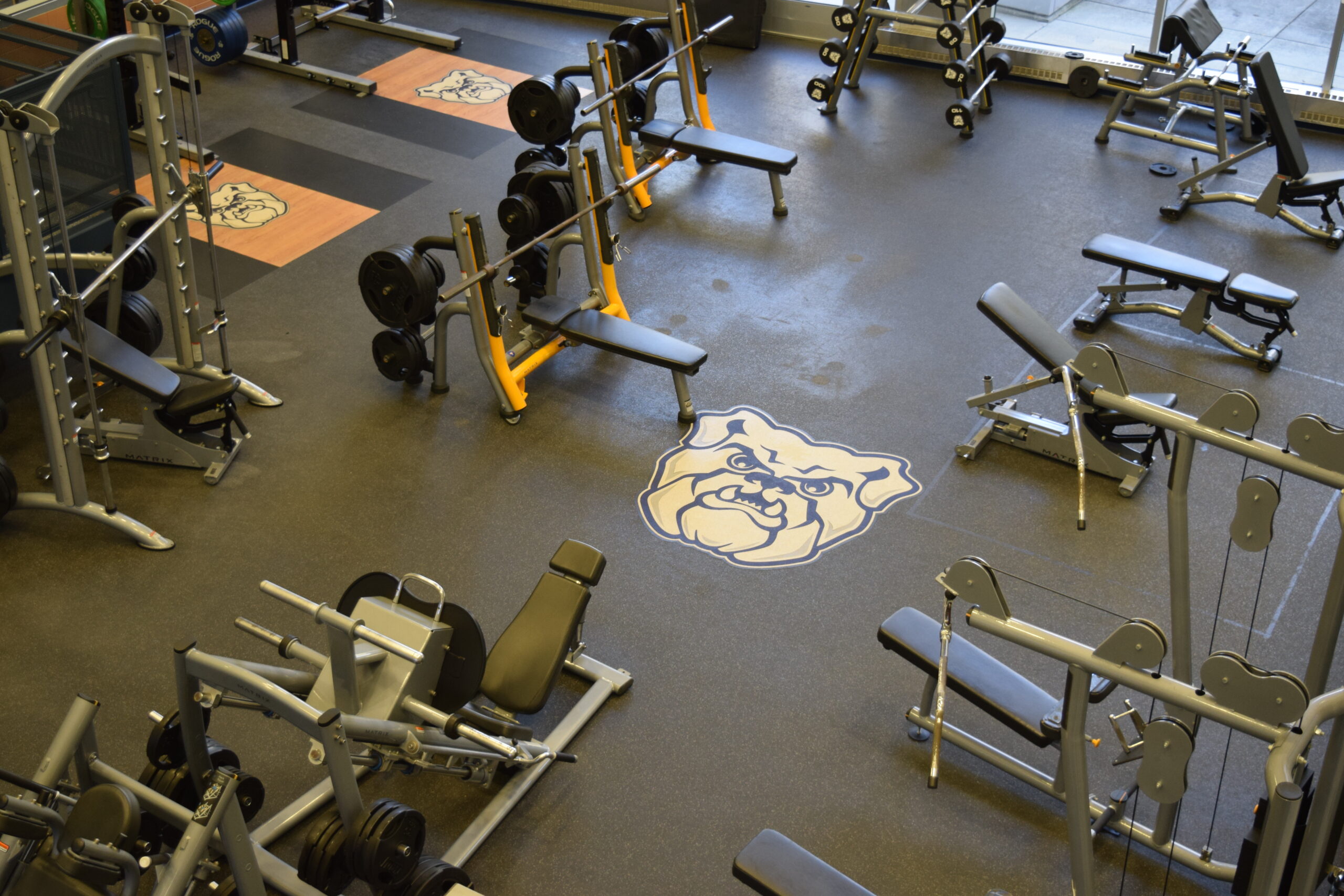 Overhead view of the workout room named The Kennel with its weights equipment and a Butler Bulldog logo on the floor.