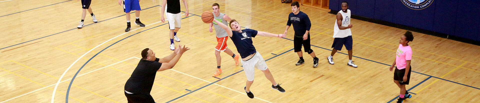 Basketball player stretches to intercept a pass as group of students play a basketball pickup game in the Butler Health and Recreation Complex gymnasium.