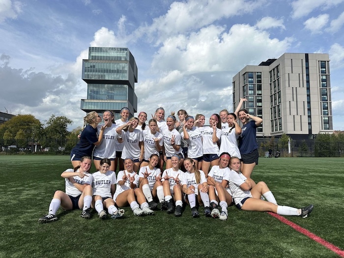 This is a photo of a group of girls. One row is sitting on the grass and the other is standing behind them. They are all wearing white and smiling.