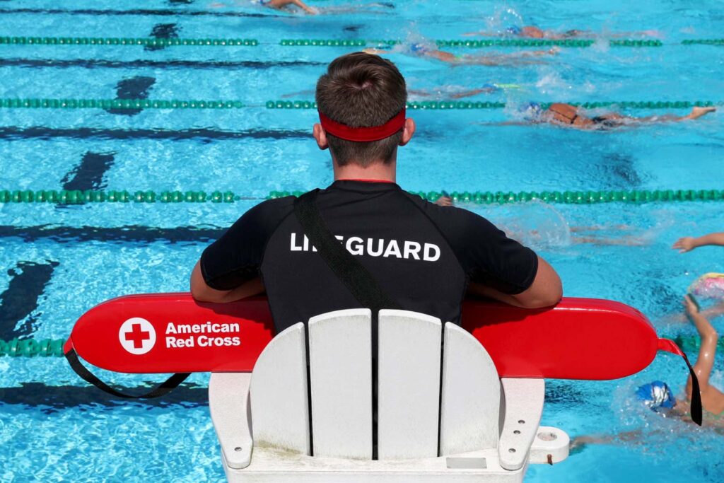 View of lifeguard from behind watching swimmers in pool from his high chair.