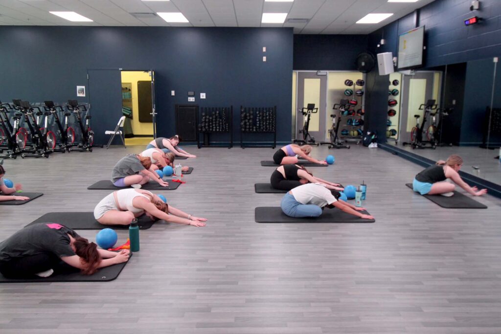 Class of people facing the same direction do stretches on exercise mats.
