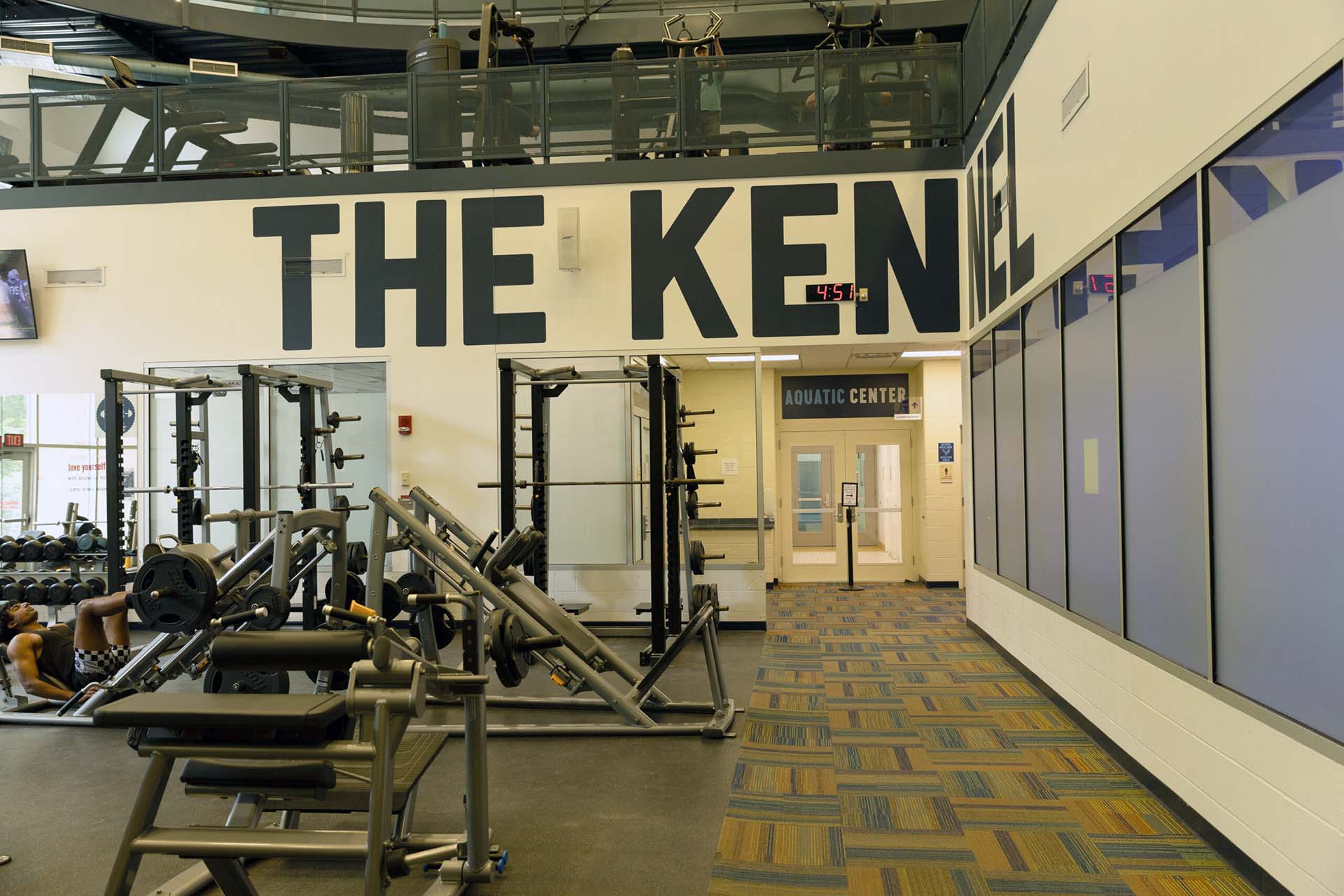 Weight room with equipment and a wall that has large letters spelling "The Kennel."