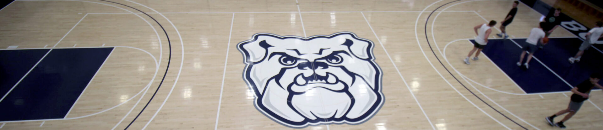 Overhead view of basketball court floor with Butler bulldog logo at center court and players on one end of the court.