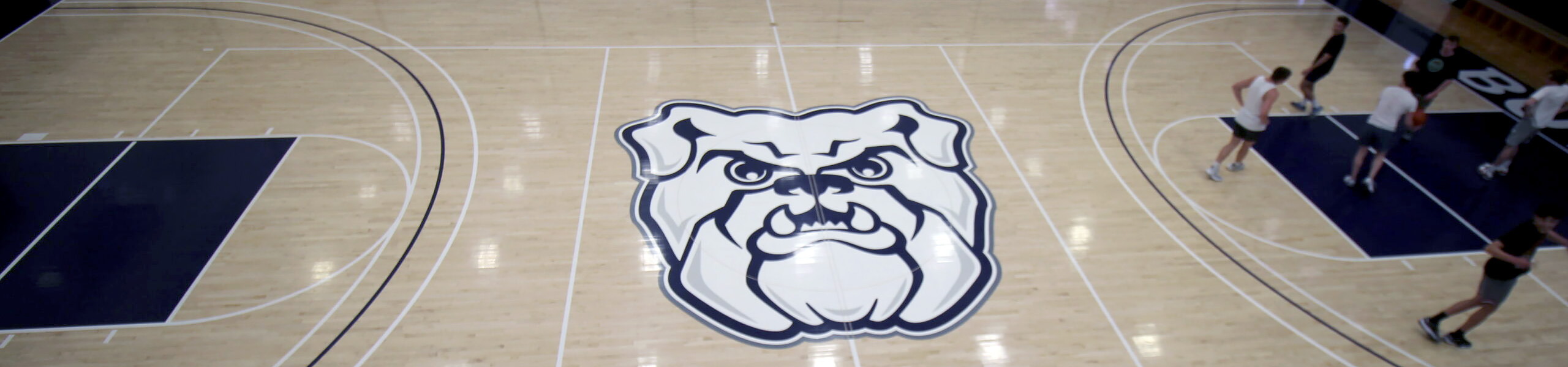 Overhead view of basketball court floor with Butler bulldog logo at center court and players on one end of the court.