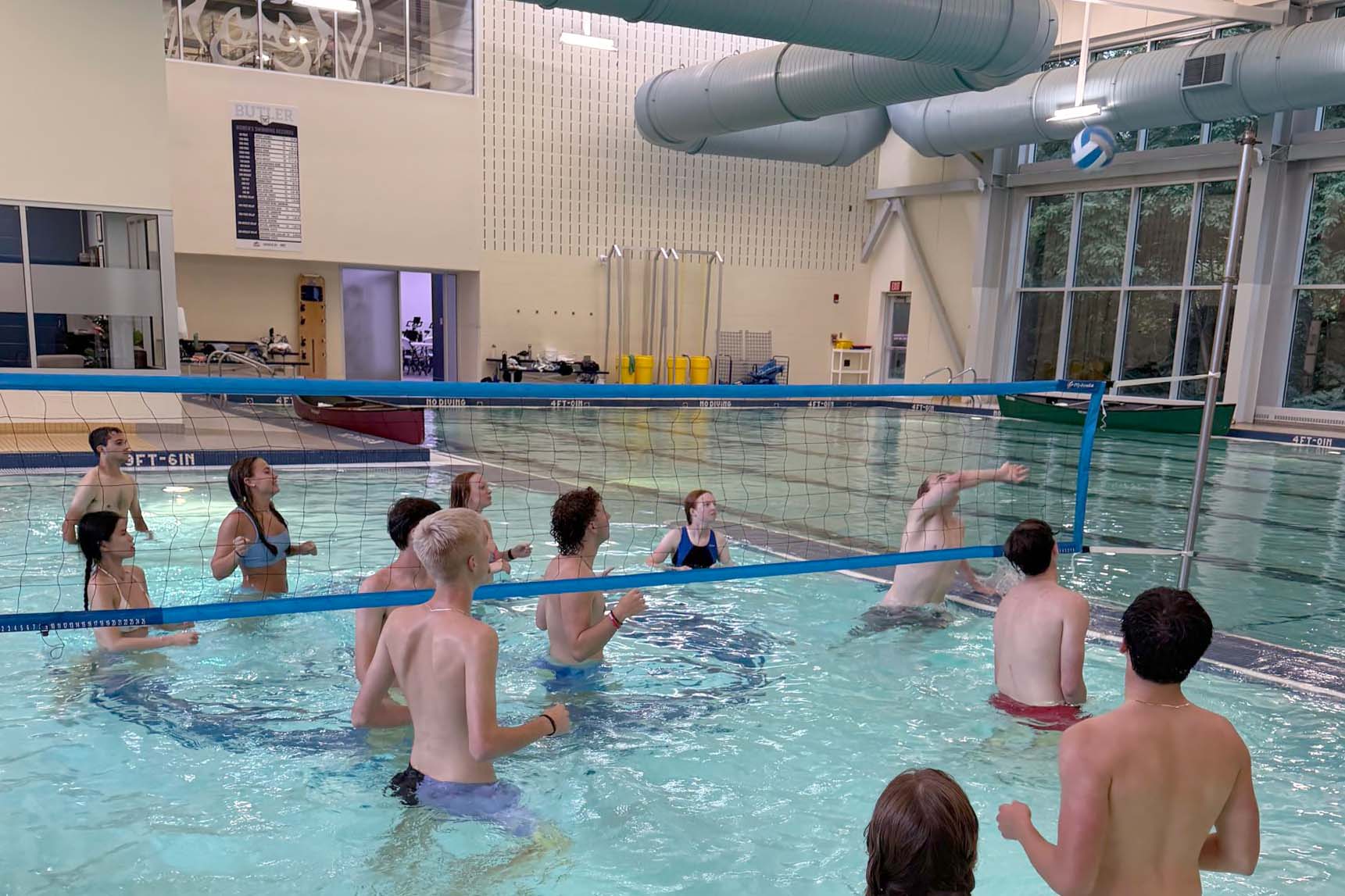 Young adults playing water volleyball watch as one player tries to save the ball from going out of bounds.