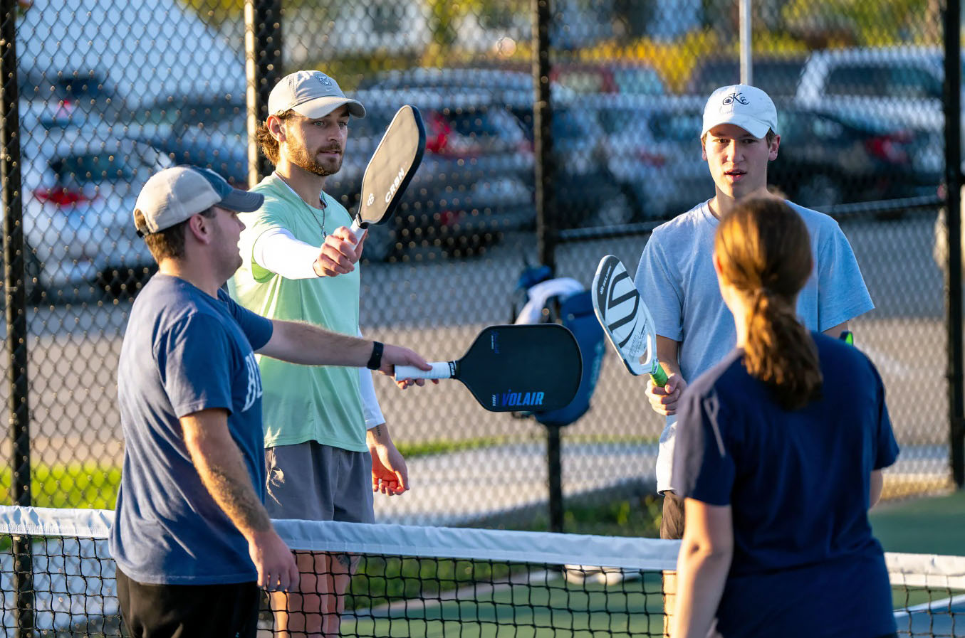 Players on the outdoor pickleball courts meet at the net and bump their paddles in a sign of sportsmanship.