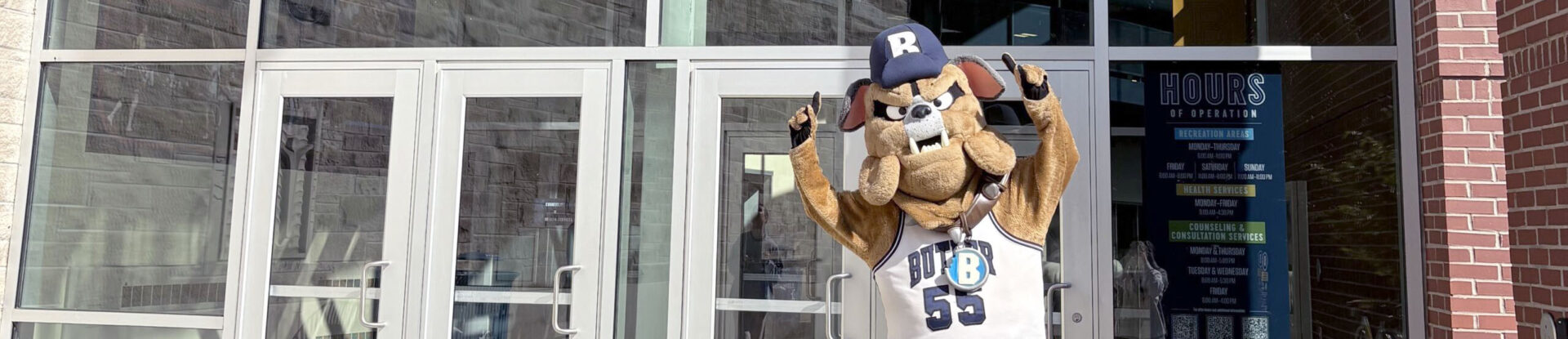 Hink mascot waving in front of entrance doors to Health and Recreation Complex.