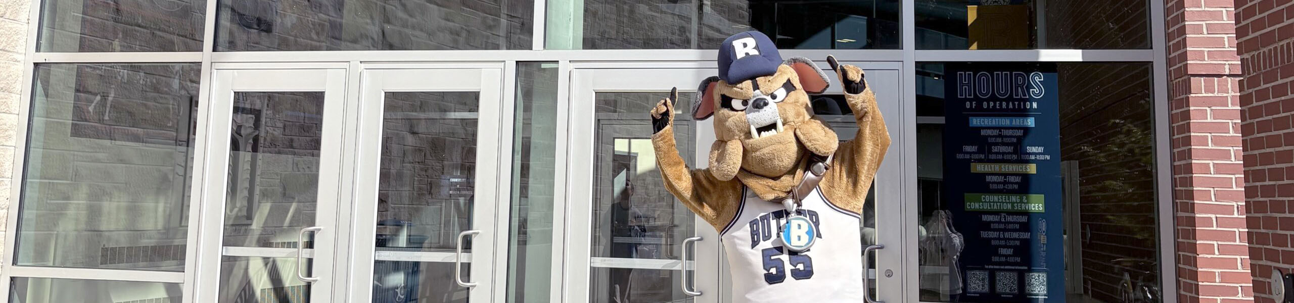 Hink mascot waving in front of entrance doors to Health and Recreation Complex.