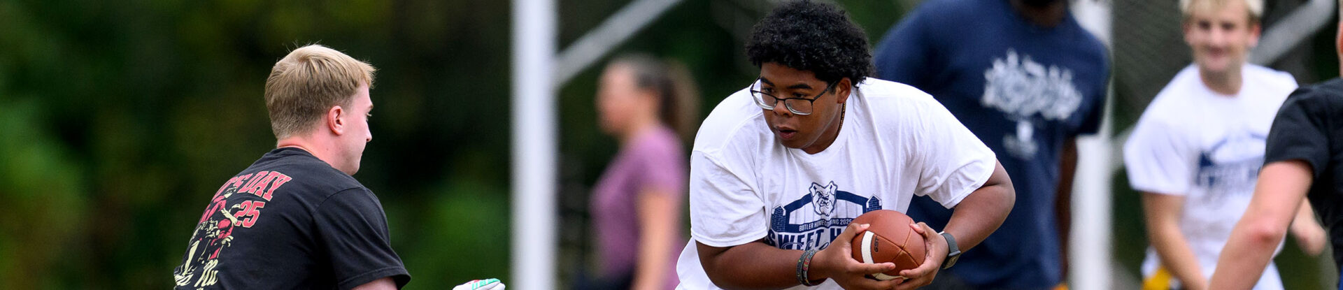 Intramural flag football runner carrying the football evades a tackle.