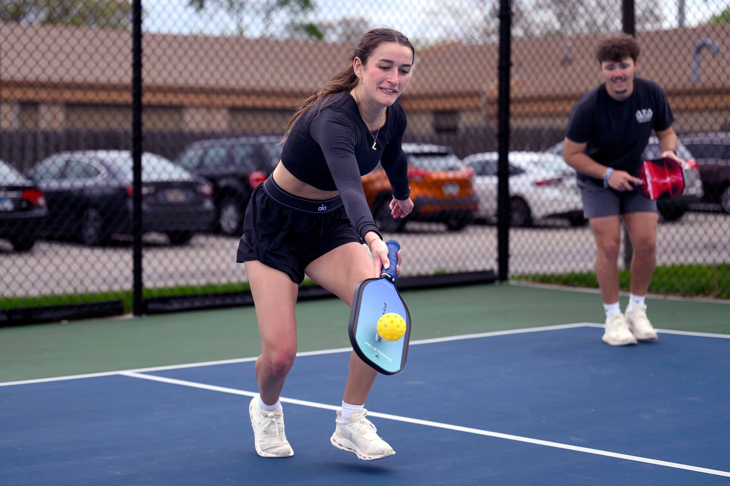 Woman playing pickleball runs and swats the ball with a low hit.