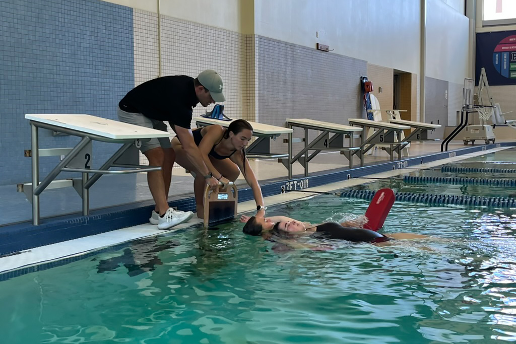 Lifeguards Steven, Emily, and Hannah performing a swim rescue and bring swimmer to pool edge.