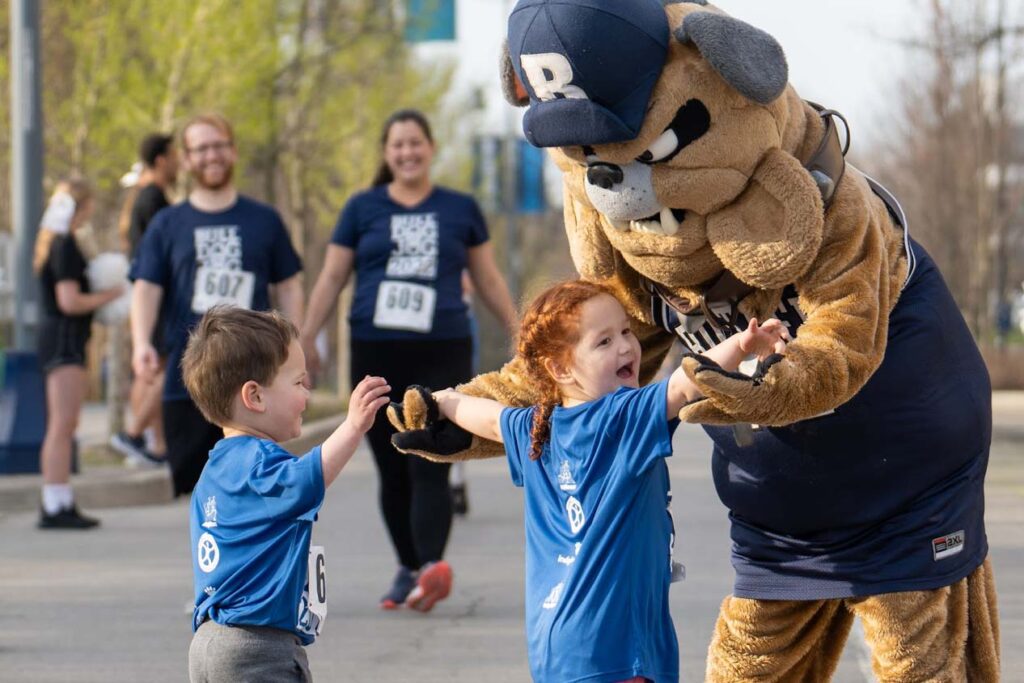 Hink the bulldog mascot leans over to hug two young children during the Bulldog Jog race event.