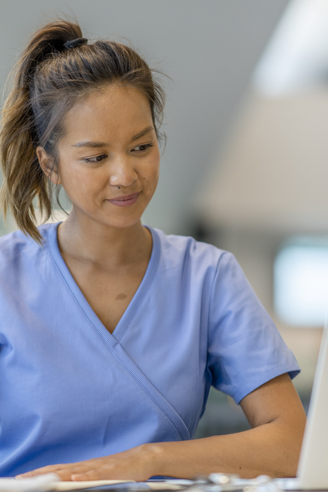A female medical student in light blue scrubs studying.