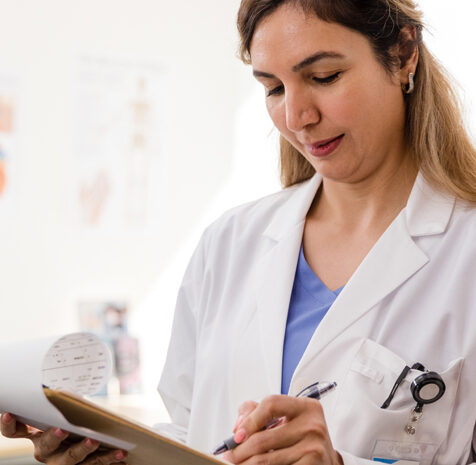 A doctor checking records on a clipboard. She is writing on the records with a pen as she does so.