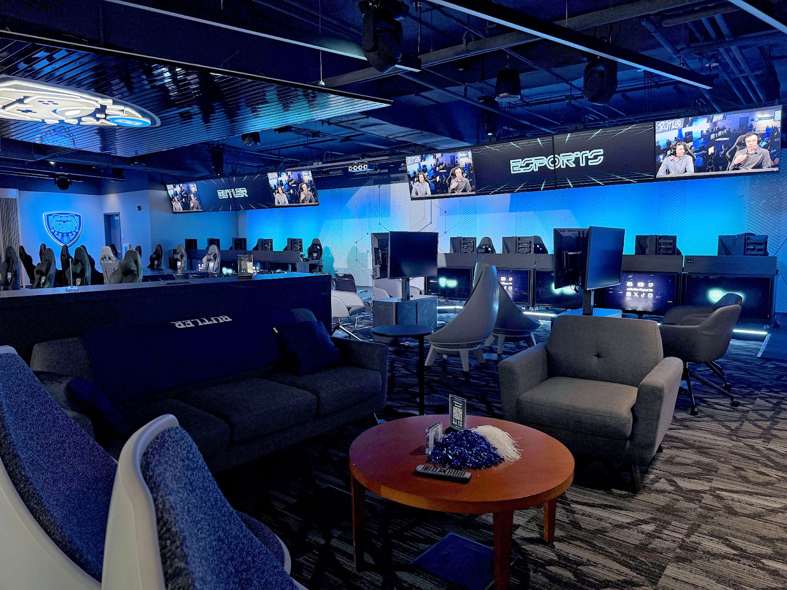 Main lounge area of Esports Park at Butler University with cushioned seating, many monitors, and low lighting.