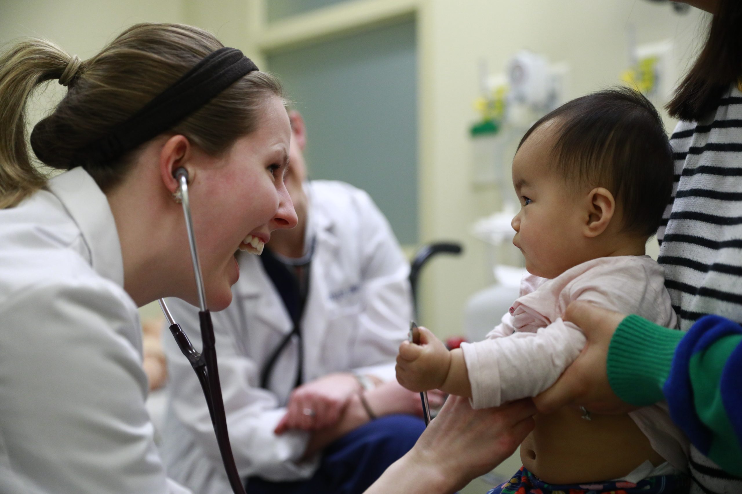A pediatric student using a stethoscope on a young baby
