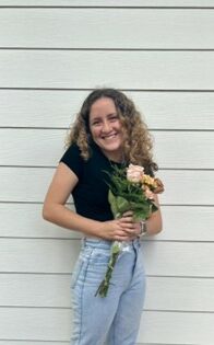 Young woman standing in front of painted panels holding flowers