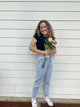 Young woman standing in front of painted panels holding flowers