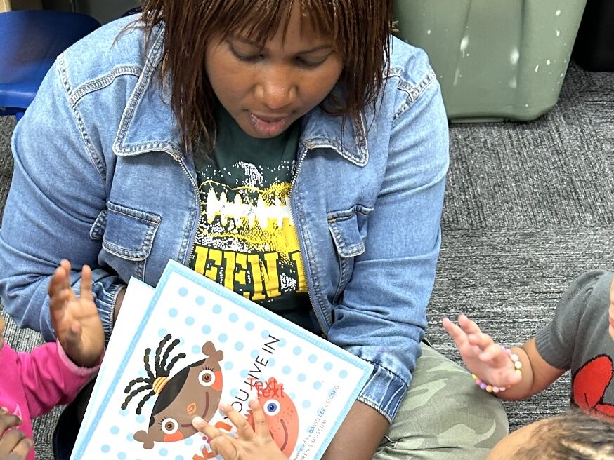 An early childhood educator sits in front of students reading a book.