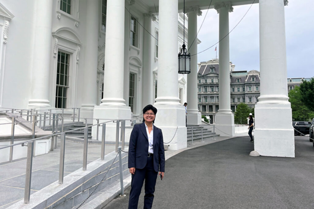Person in suit smiles in front of White House entrance steps.