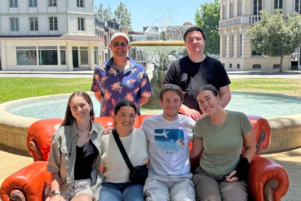 Butler students and faculty sit on couch prop from TV show "Friends" and stand in front of the fountain from the show on the Warner Brothers Studios back lot in Los Angeles.