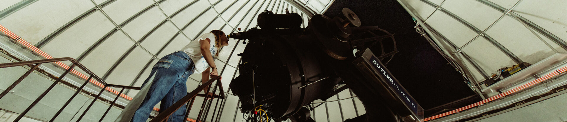 Female college student looks at night sky through large telescope in an observatory.